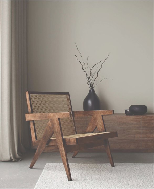 A cane-seated lounge chair beside a low walnut console holding a dark stoneware vase of bare branches.